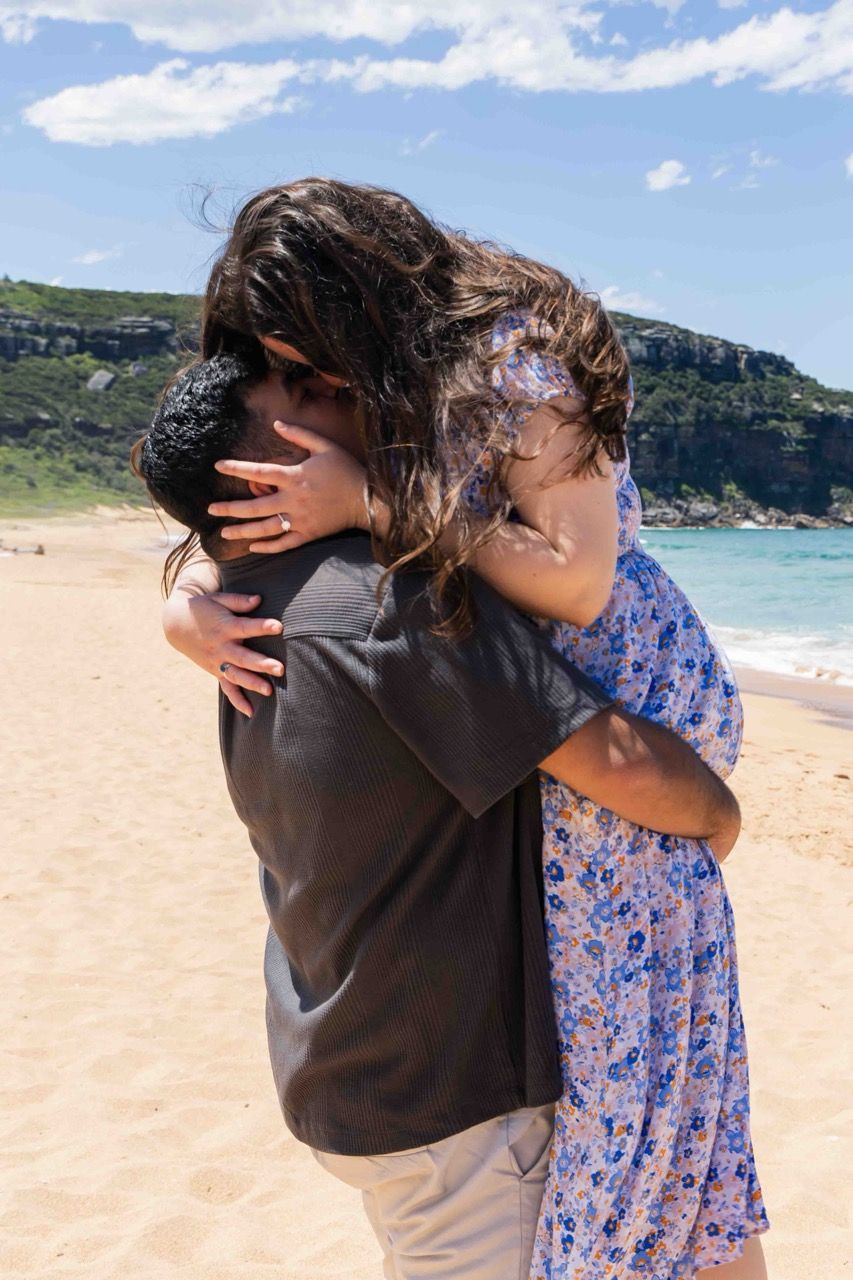 The couple embrace on the beach under a blue sky