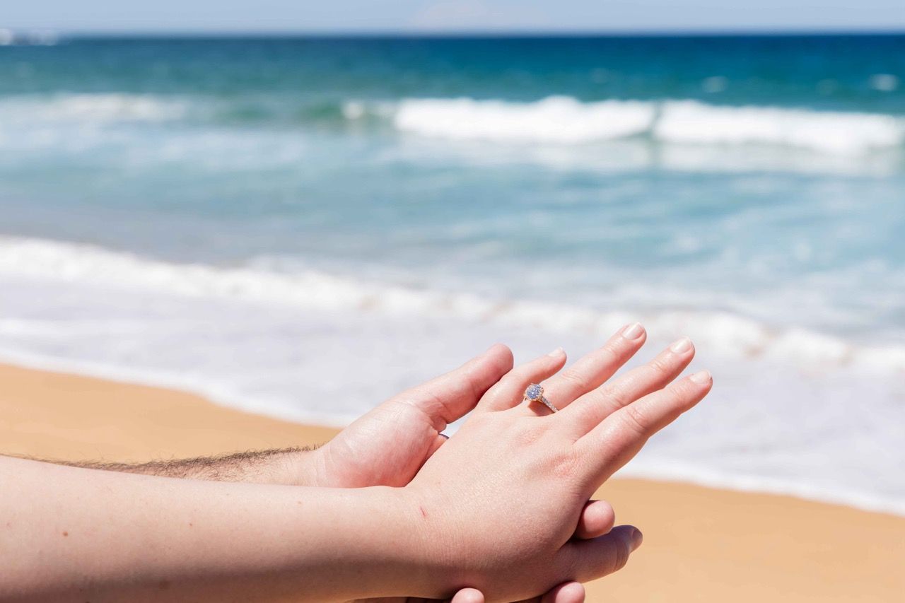 Hands held together showing the engagement ring against the surf