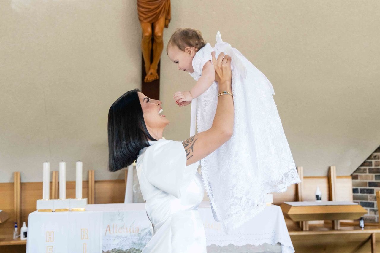 A mother lifts her baby in a white gown in front of the altar