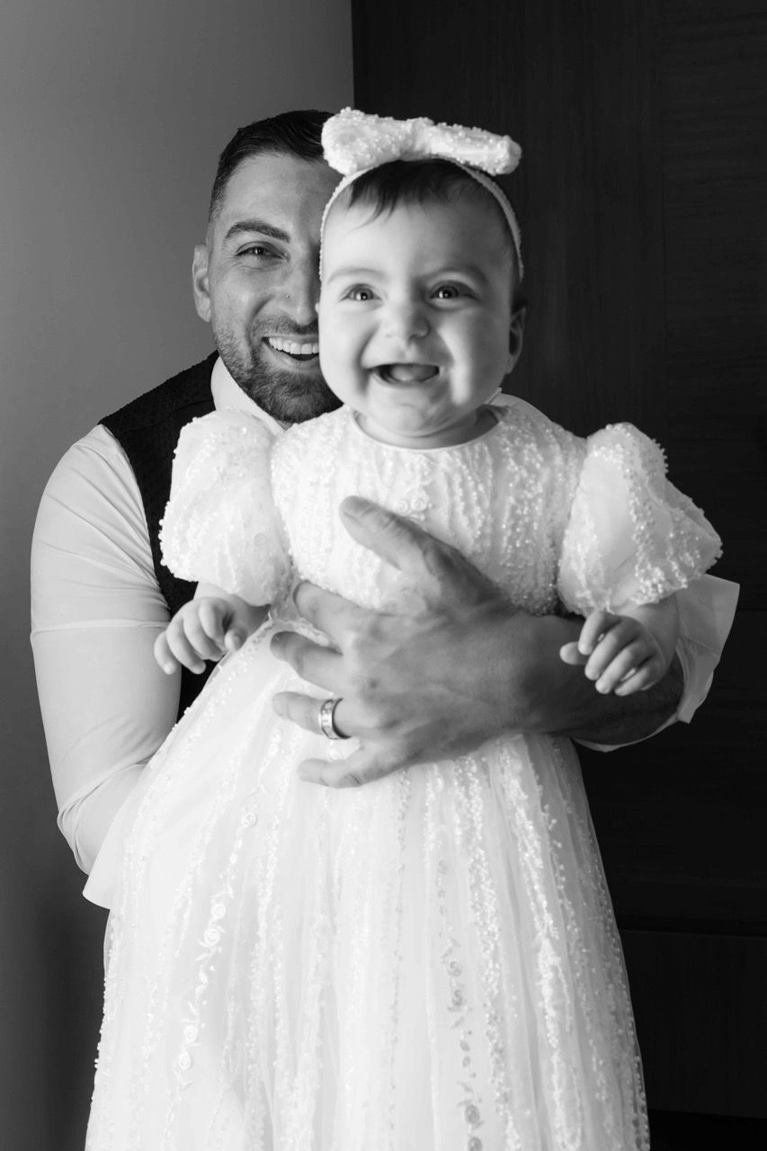 A baby in a bow laughs in her dad’s arms