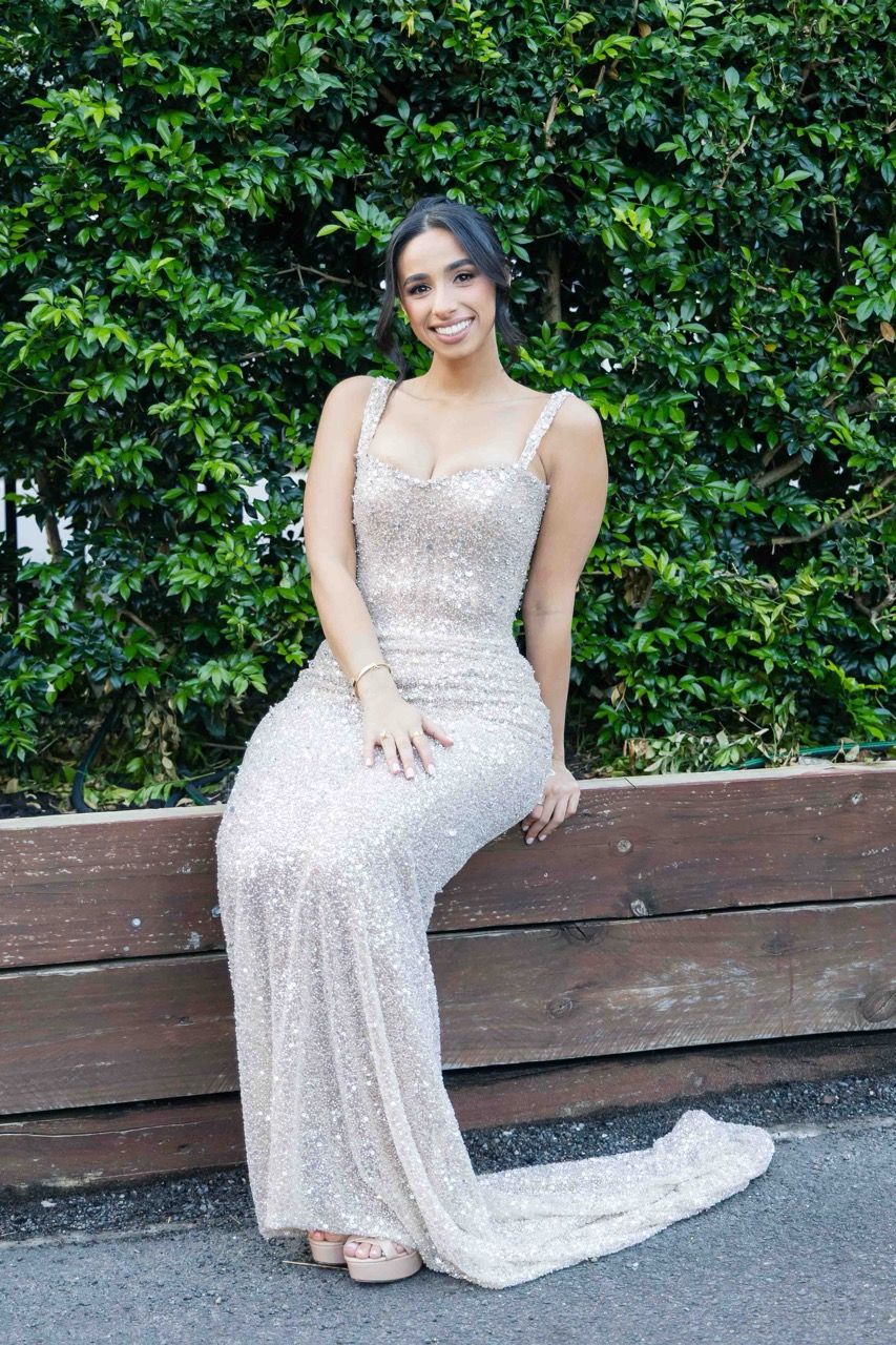 The bride-to-be sits on a ledge in front of greenery