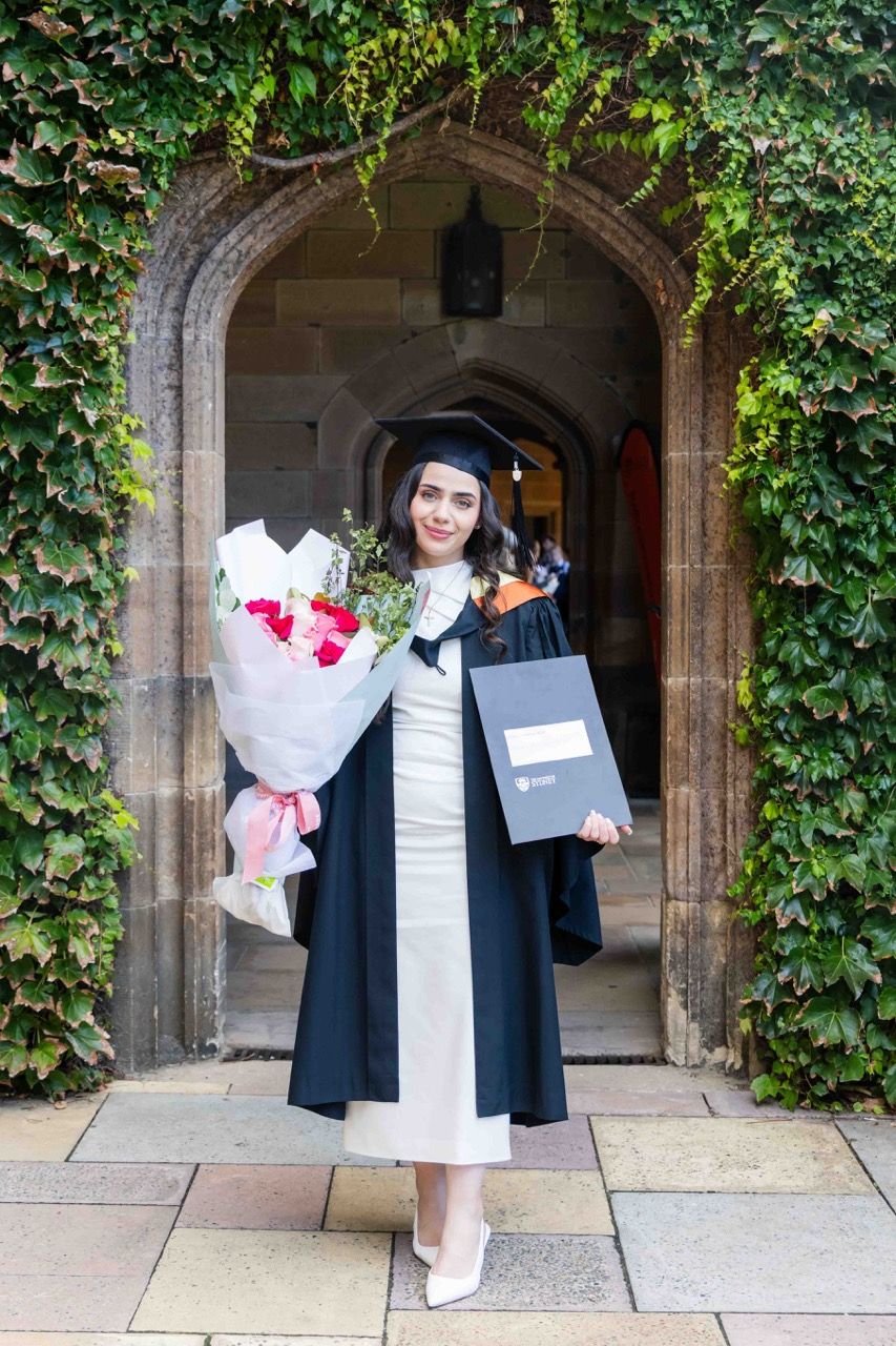 A graduate stands in an ivy-covered sandstone archway