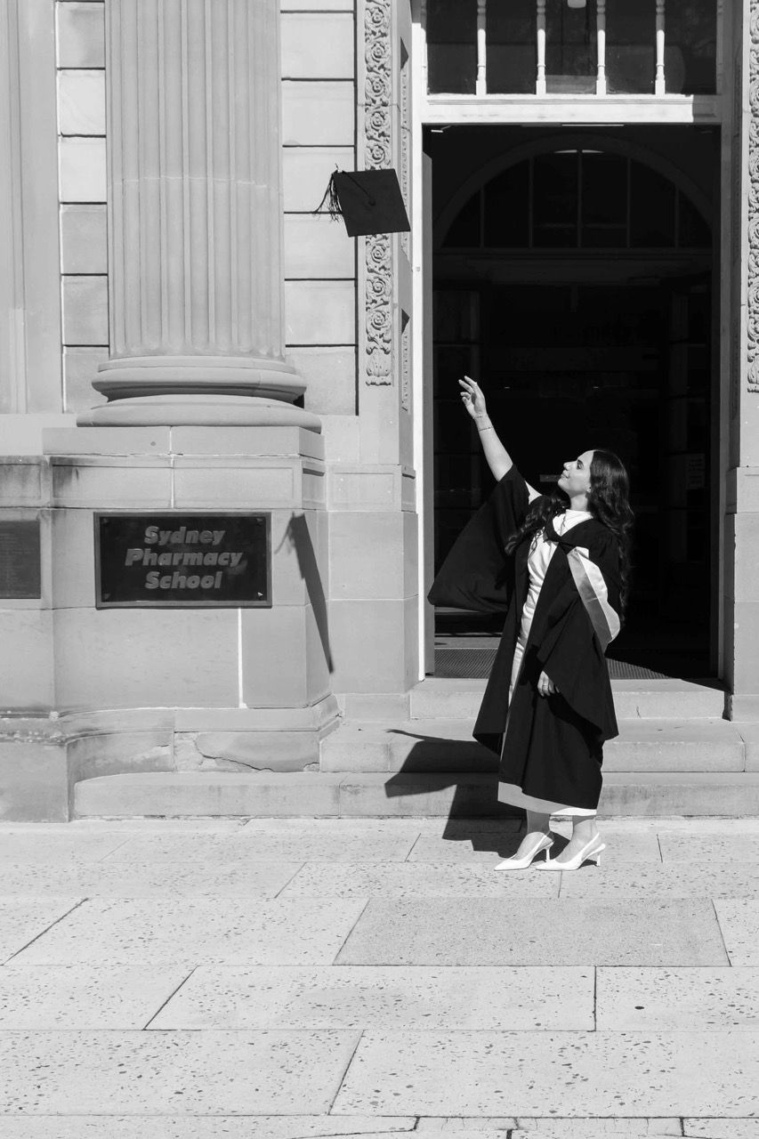 A graduate points up at the pharmacy school sign