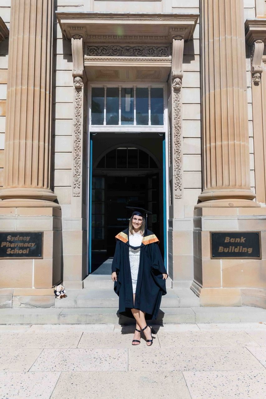 A graduate sits on the steps of a columned sandstone building