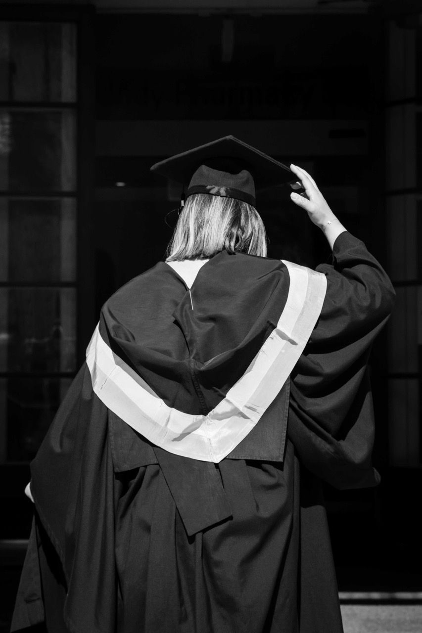 A graduate adjusts her cap, seen from behind