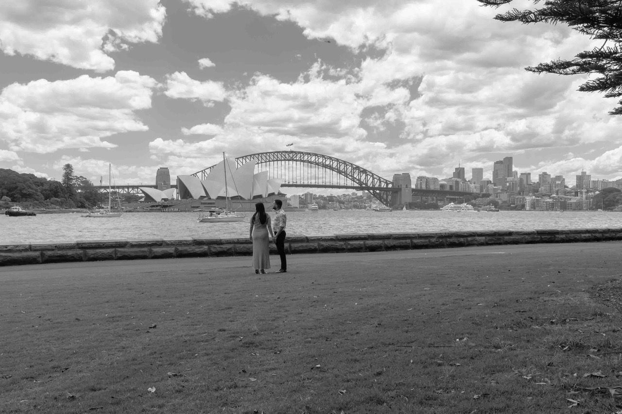 The couple stand on the foreshore with the Harbour Bridge behind