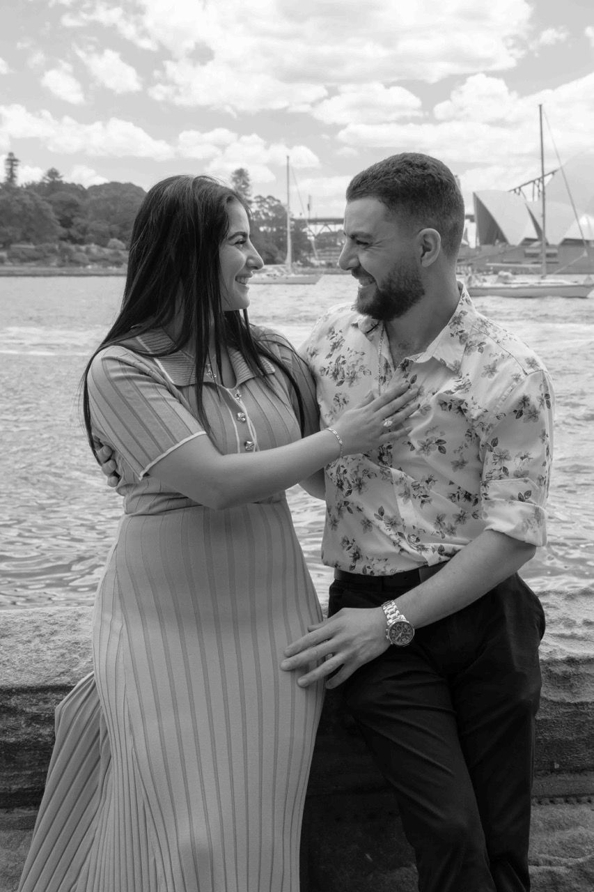 The newly engaged couple smile at each other by the water